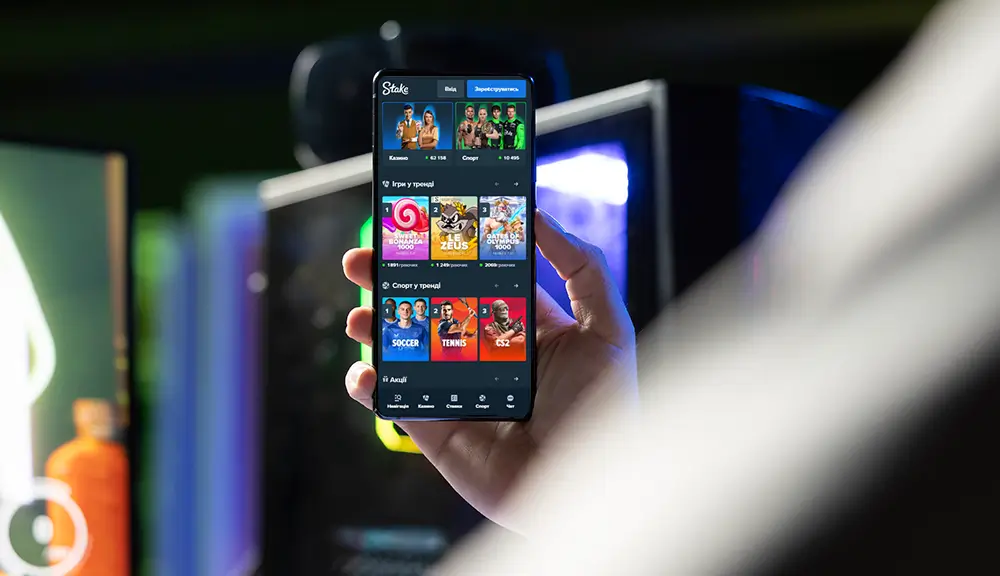 Гравець тримає смартфон з відкритим додатком Stake Casino — слоти, спорт, live-ігри